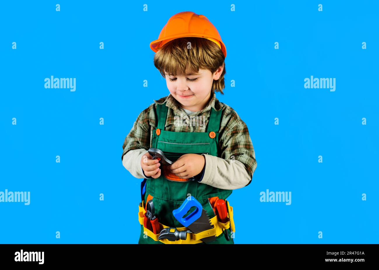 Little child boy in safety helmet and toolbelt with pipe wrench. Kid in