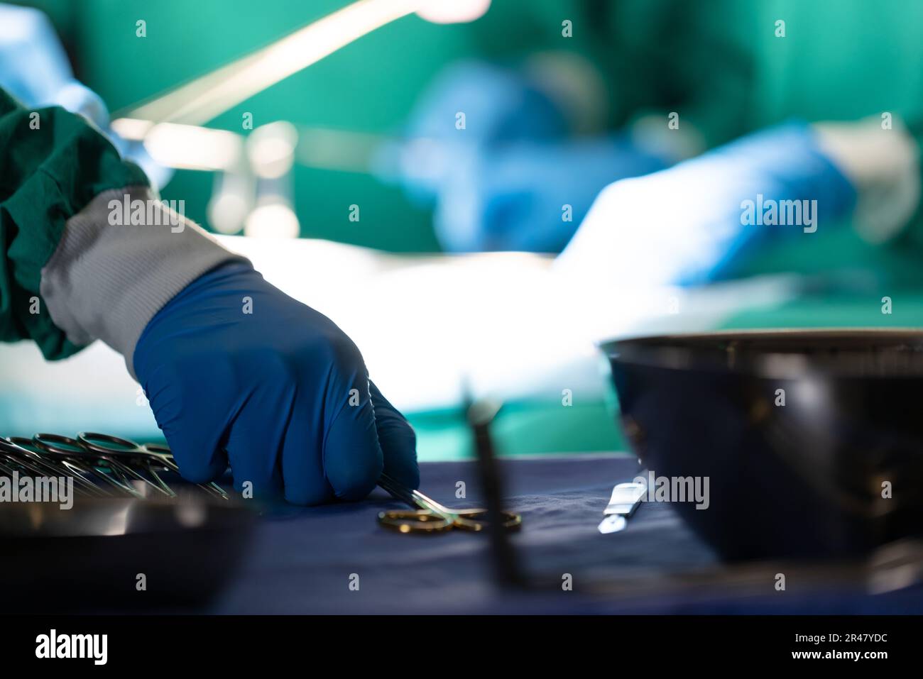 Gloved hand of surgeon picking up surgical tool during operation on