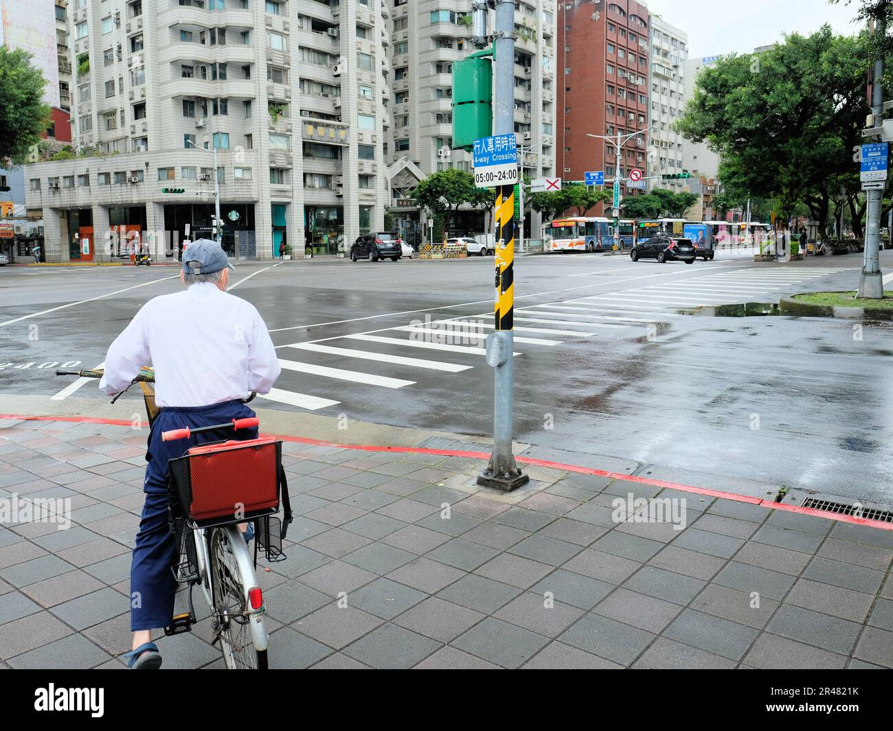 Bicycle rider stopped at a traffic light with a four way crossing sign on metal pole; buses, cars, and motor scooters, Da'an District, Taipei, Taiwan. Stock Photo