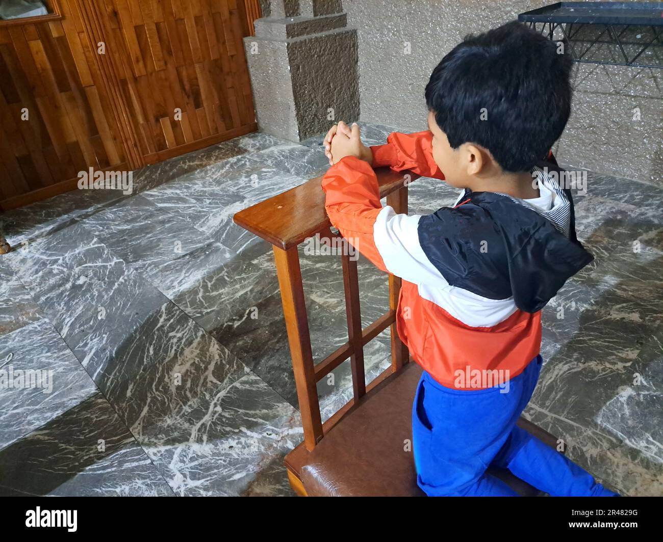 9-year-old Latino boy kneeling inside a chapel prays to God and saints ...