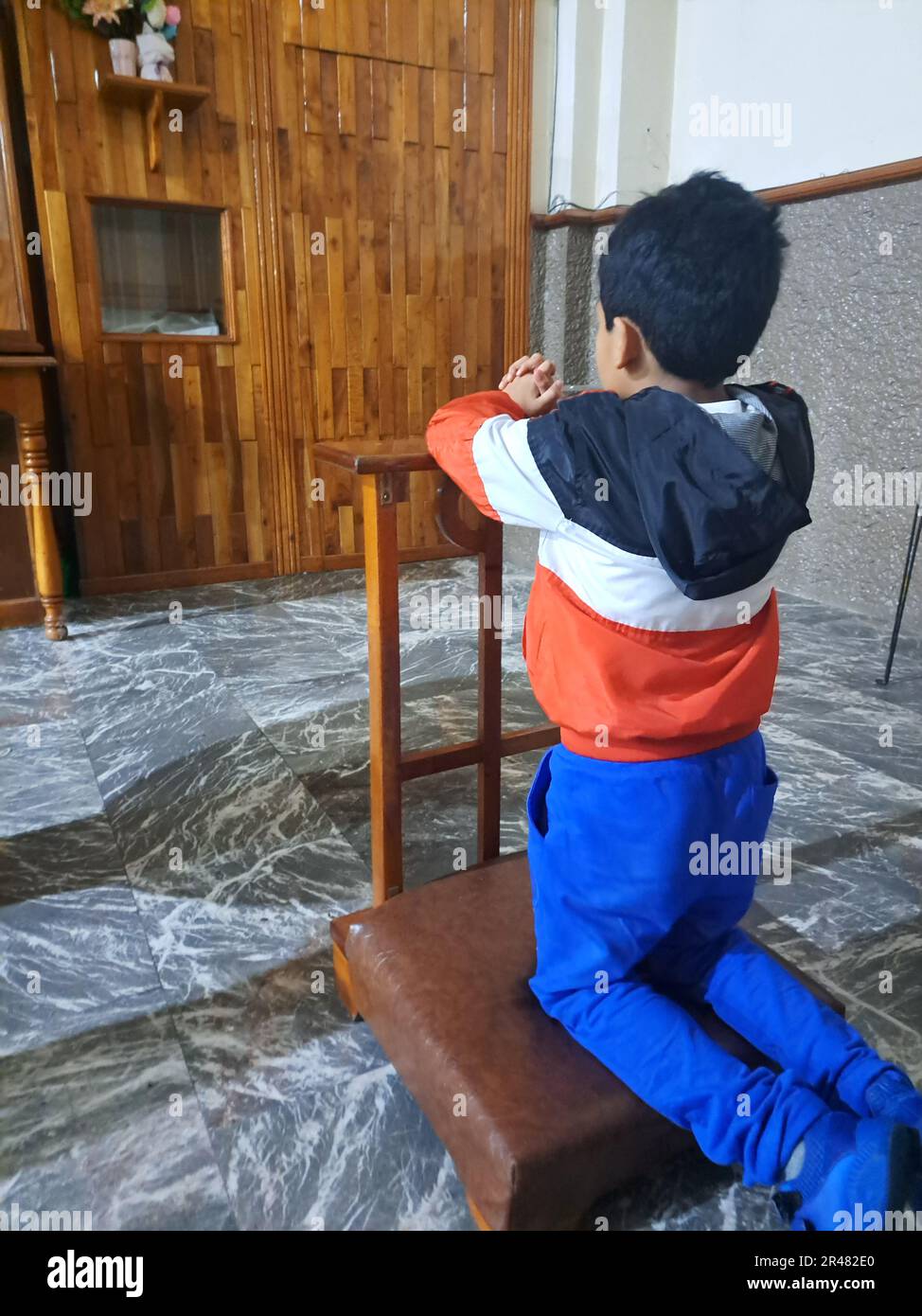 9-year-old Latino boy kneeling inside a chapel prays to God and saints ...