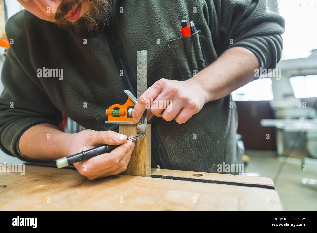 Hands of male carpenter drawing line using marker and ruler before