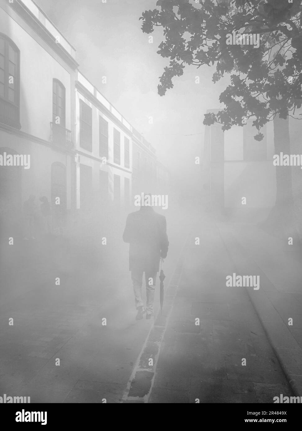 A vertical shot of a silhouette of an older male with an umbrella walking in the mist Stock Photo