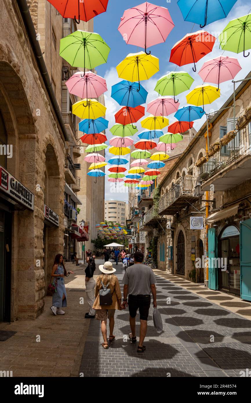 Pedestrians walk under colorful umbrellas suspended above Yoel Solomon