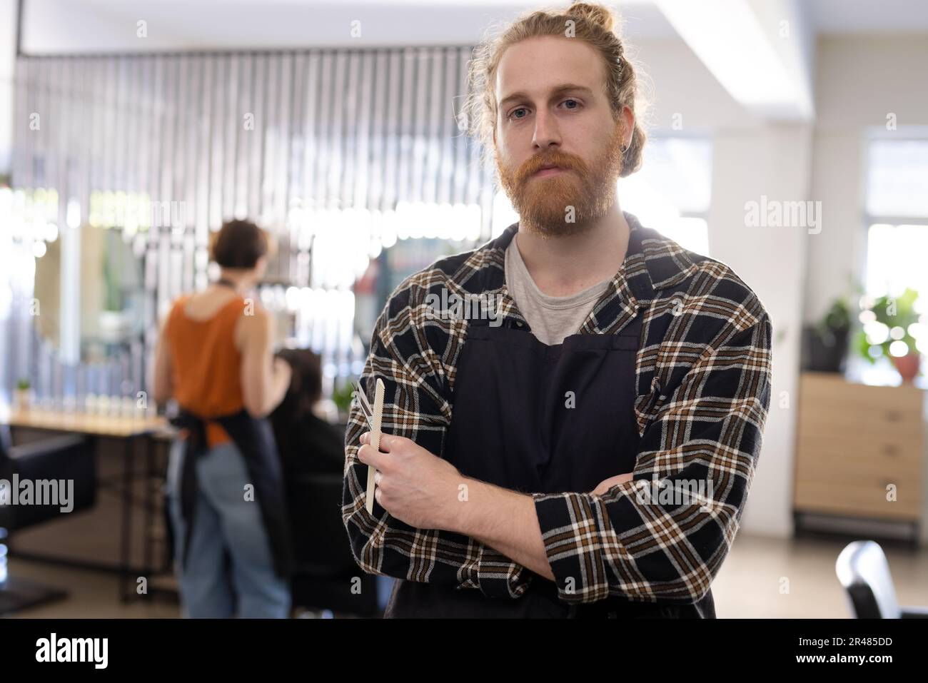 Portrait of caucasian male hairdresser in apron holding scissors and comb at hair salon, copy space Stock Photo