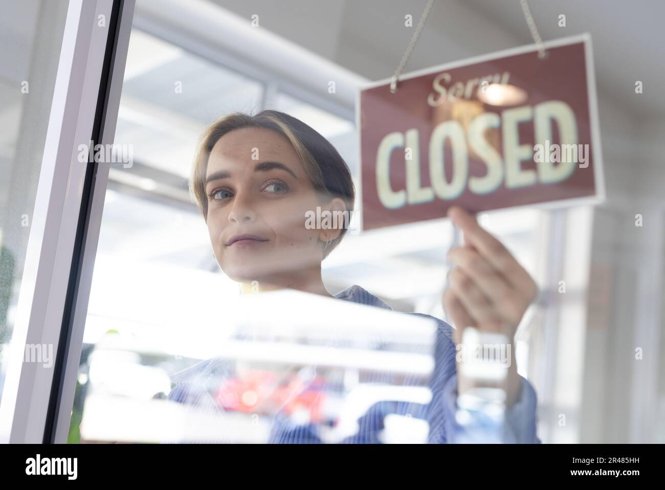 Happy caucasian female hairdresser turning sign to closed on glass door of hair salon Stock Photo