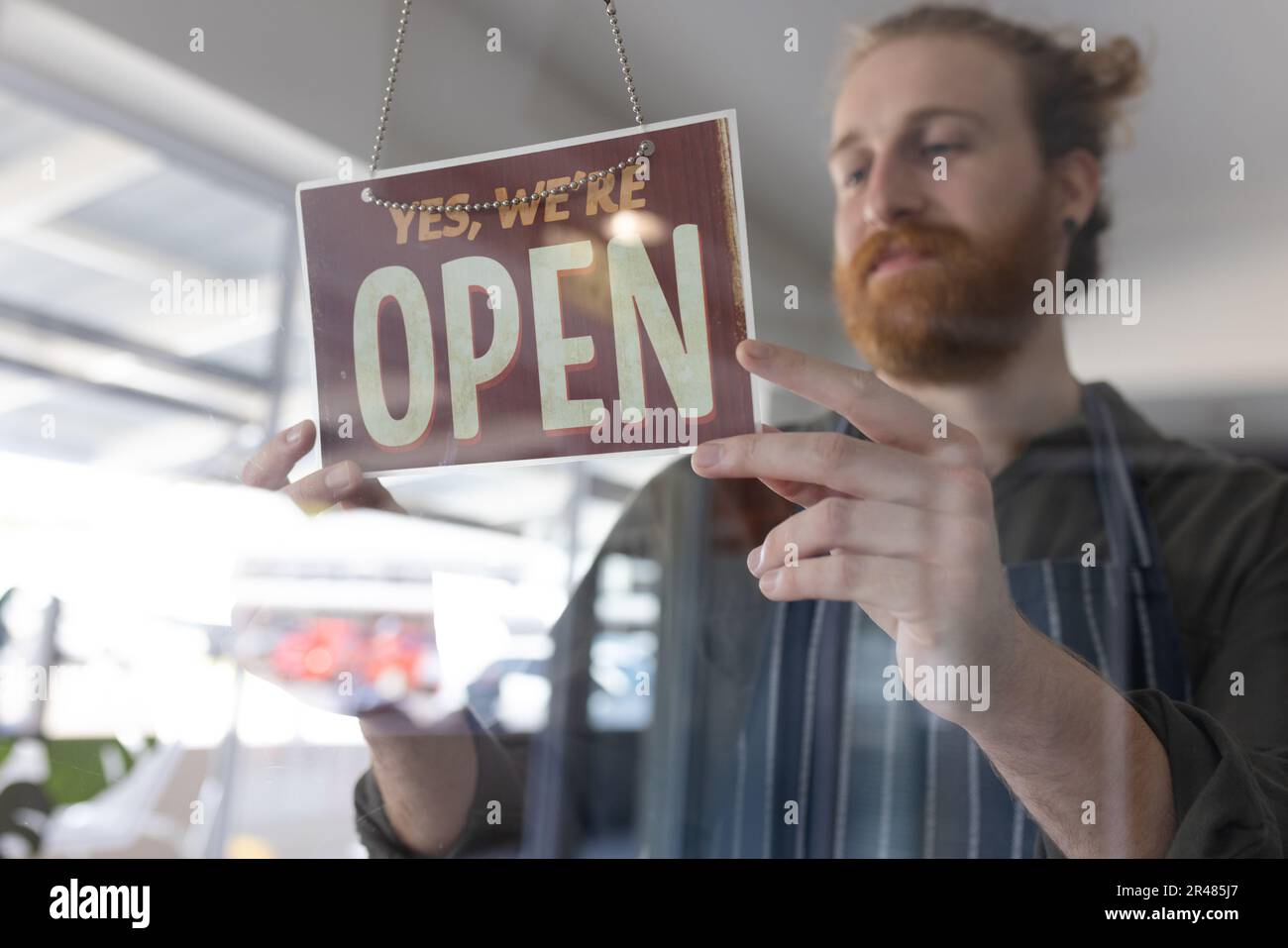 Happy caucasian male hairdresser turning sign to open on glass door of hair salon Stock Photo