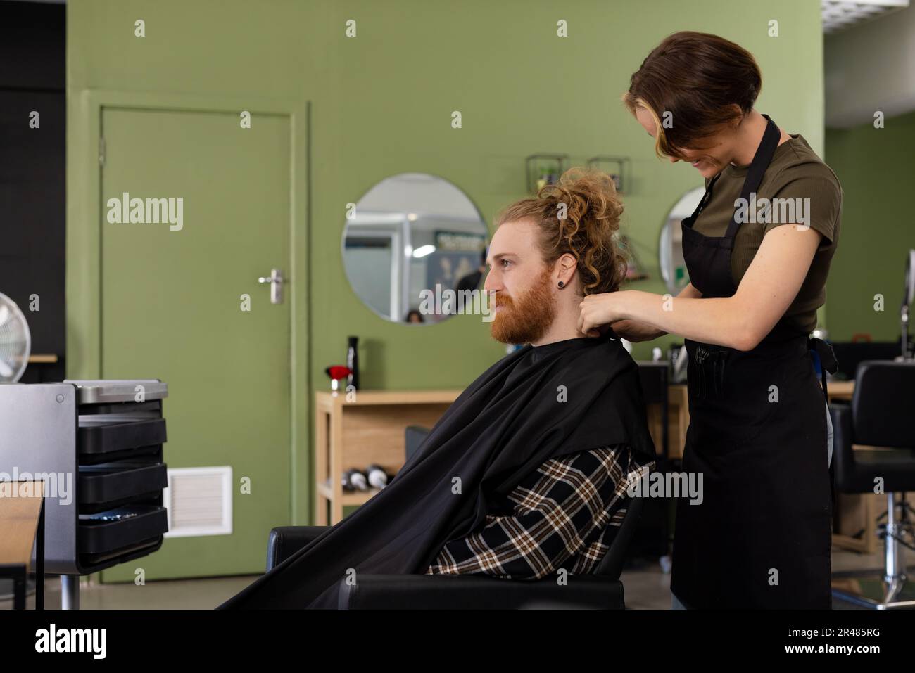 Focused caucasian female hairdresser cutting hair of male client in hair salon Stock Photo