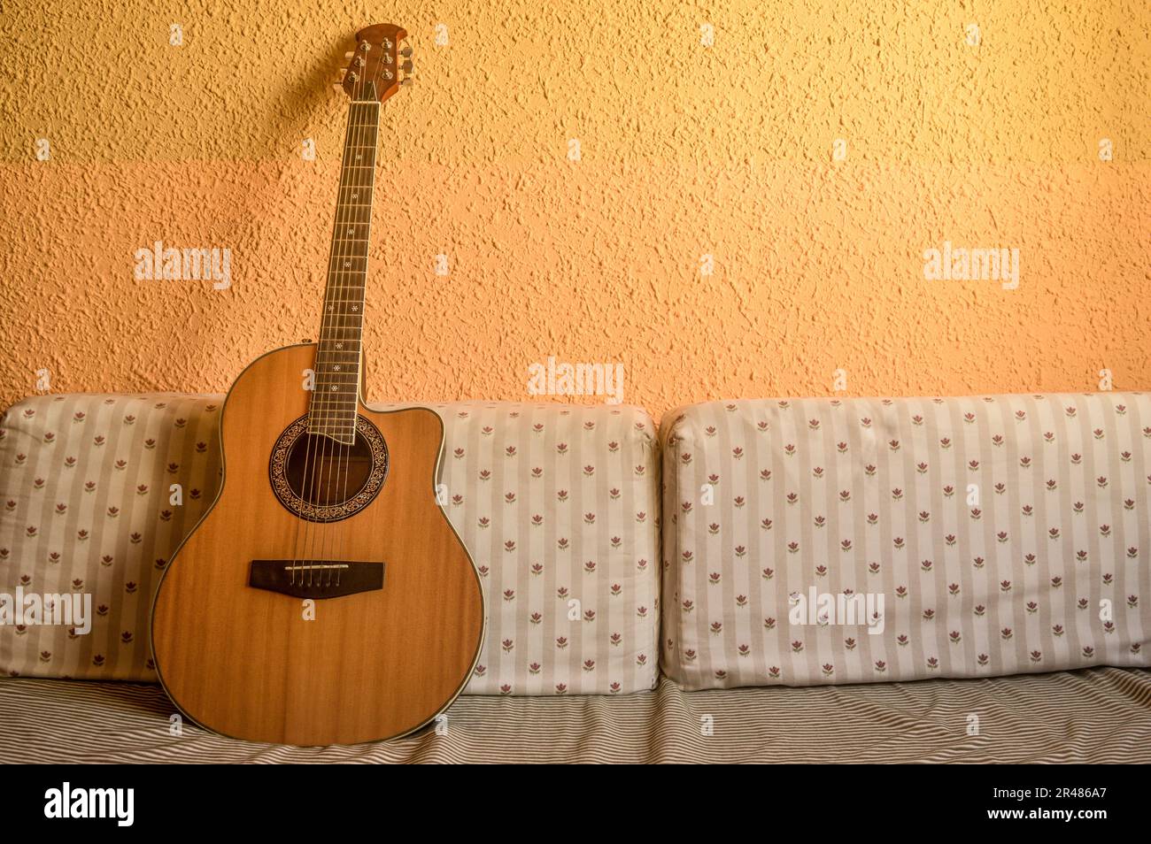 An acoustic guitar sits atop a bed full of fluffy pillows, illuminated ...