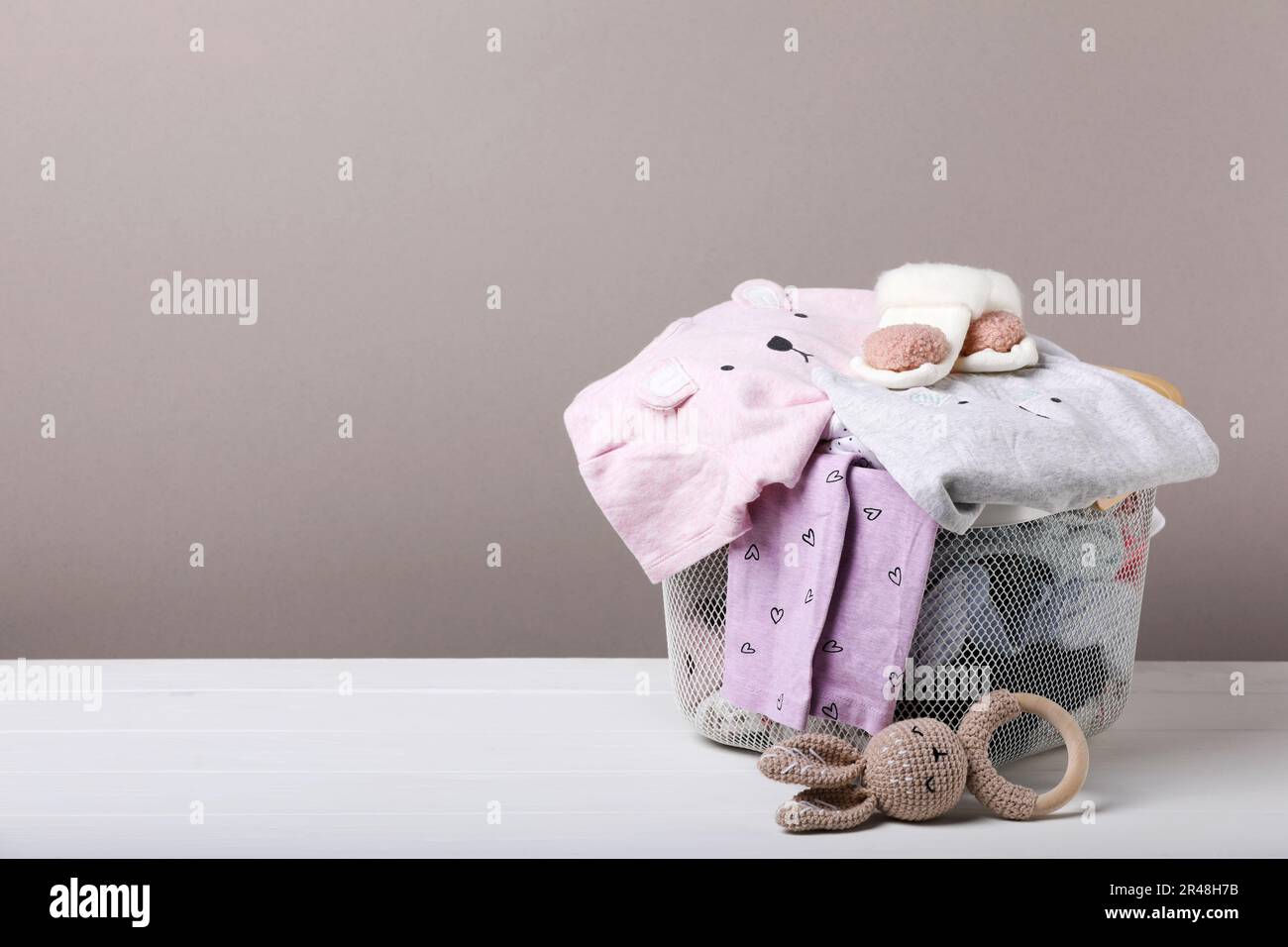 Laundry basket with baby clothes and soft toy on white wooden table ...