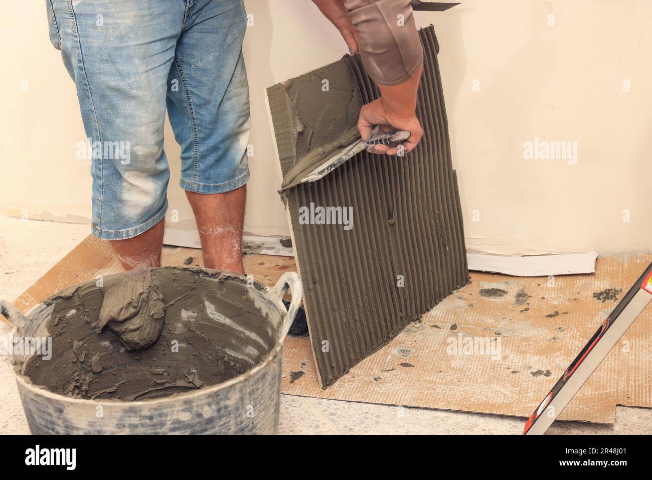 Worker spreading adhesive mix over tile with spatula, closeup Stock Photo