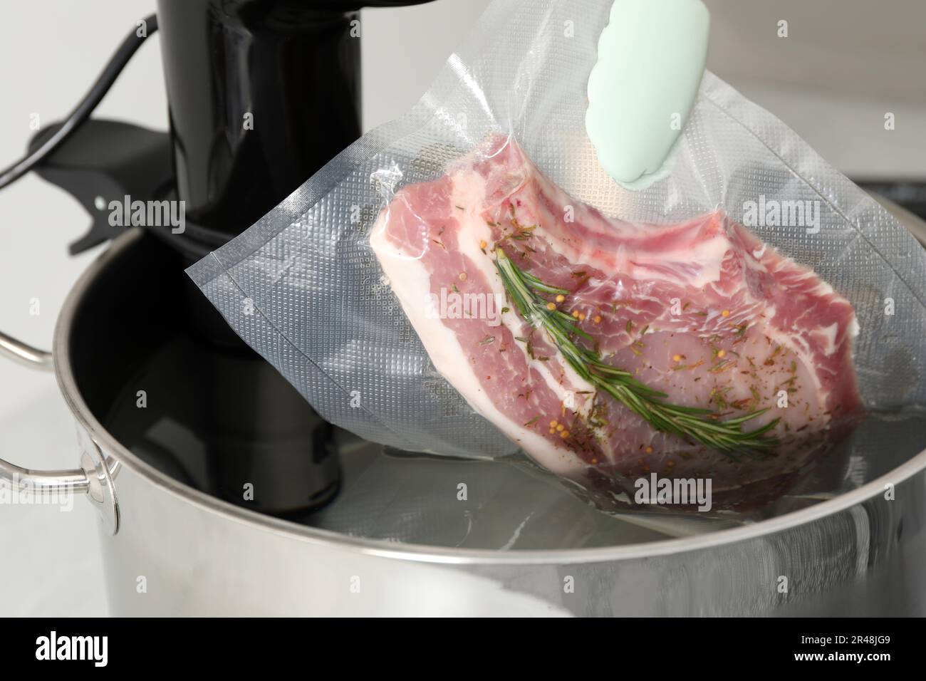 Woman putting vacuum packed meat into pot with sous vide cooker in