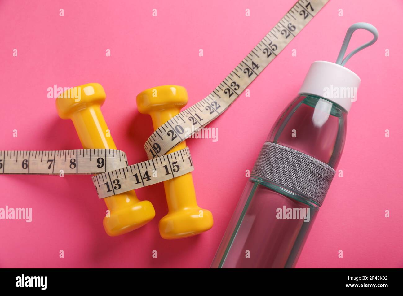 Measure tape with dumbbells and weight scale on the pink