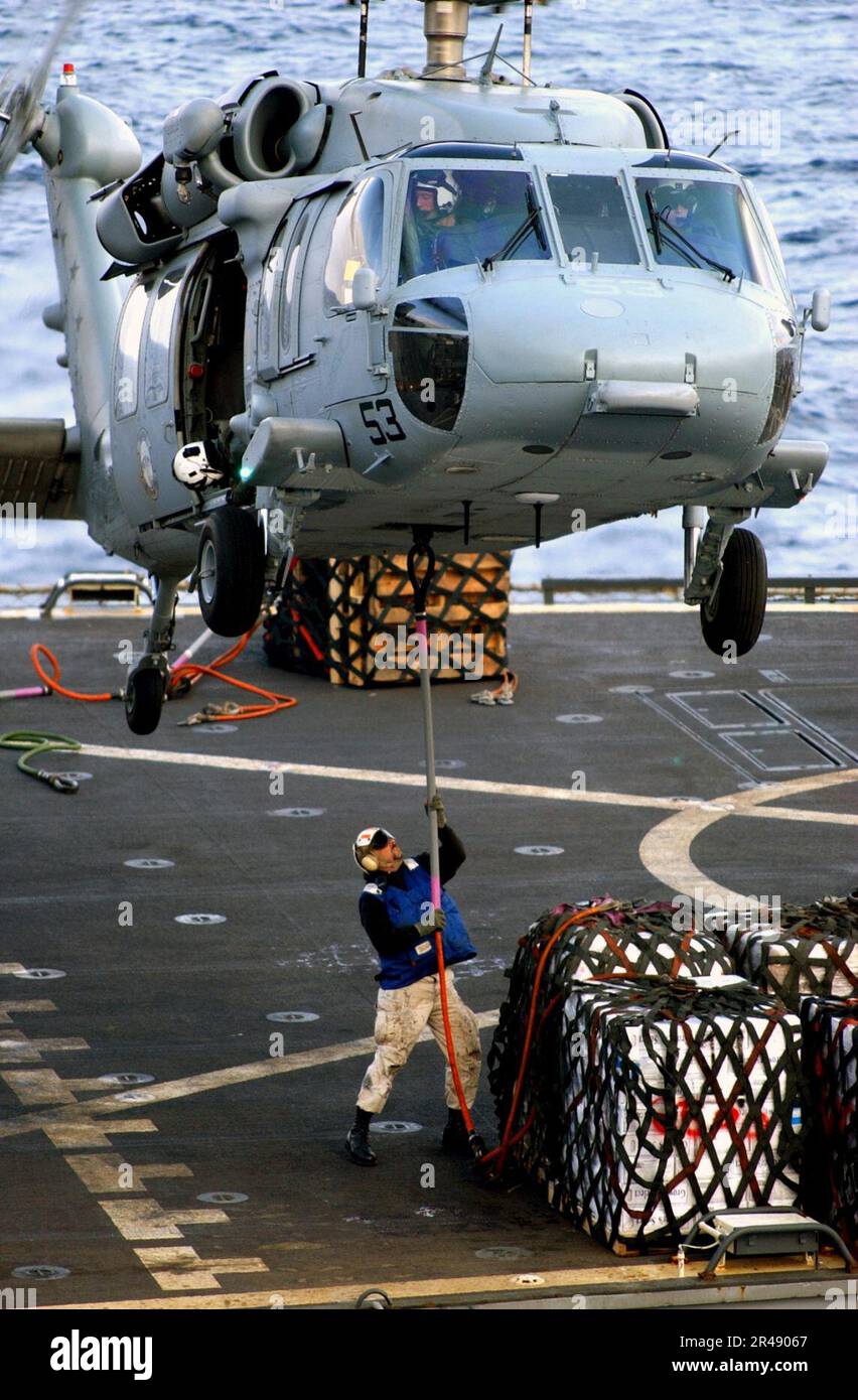 US Navy A Sailor assigned to the combat stores ship USNS San Jose (T-AFS 7) attaches a hoist line to the bottom of an SH-60 ''Seahawk'' Stock Photo