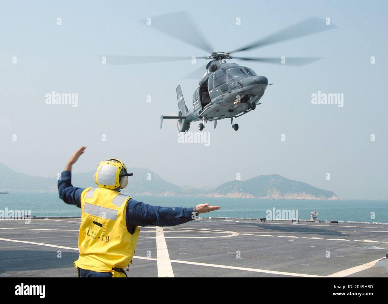 US Navy Landing Signalman Enlisted (LSE) Boatswain's Mate 1st Class from Seattle, Wash., signals an EC-155 Dauphin helicopter from the Hong Kong Government Flying Service to depart the flight deck Stock Photo