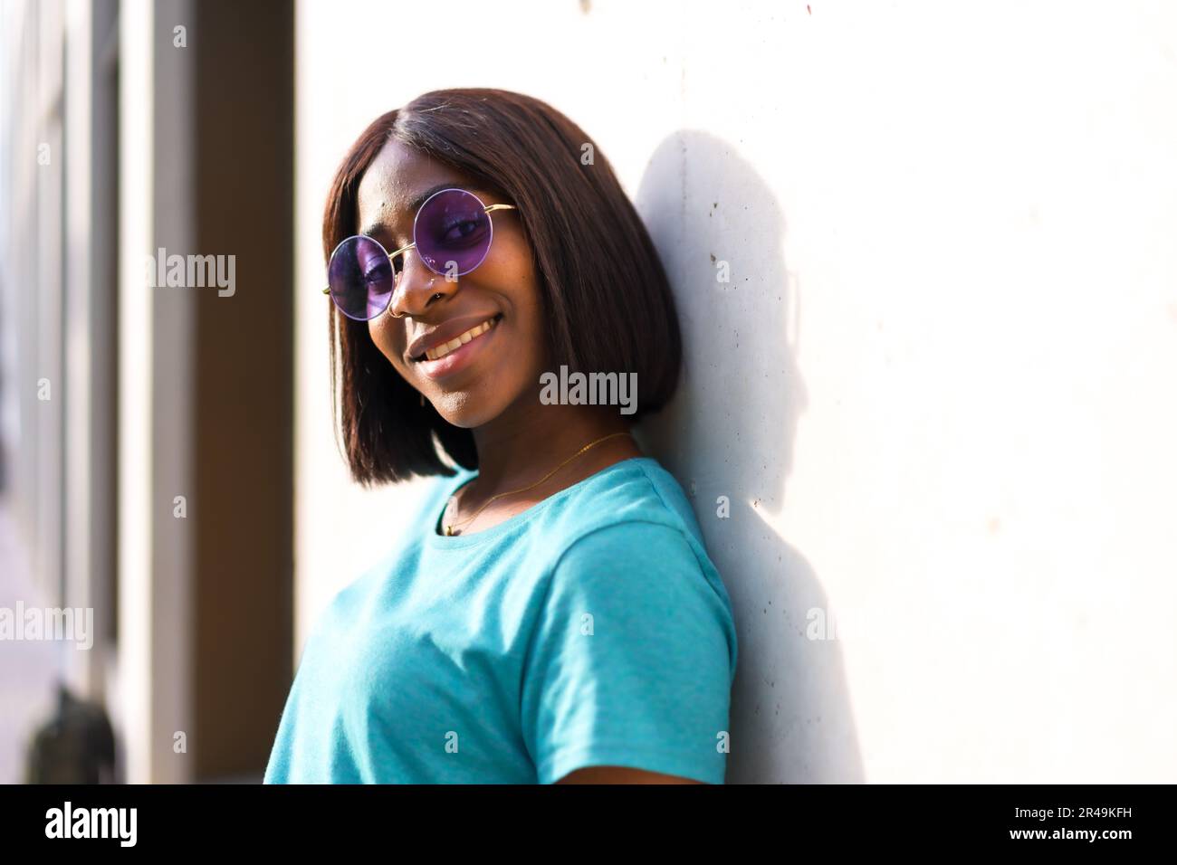 A stylish young black female in sunglasses standing against a wall in ...