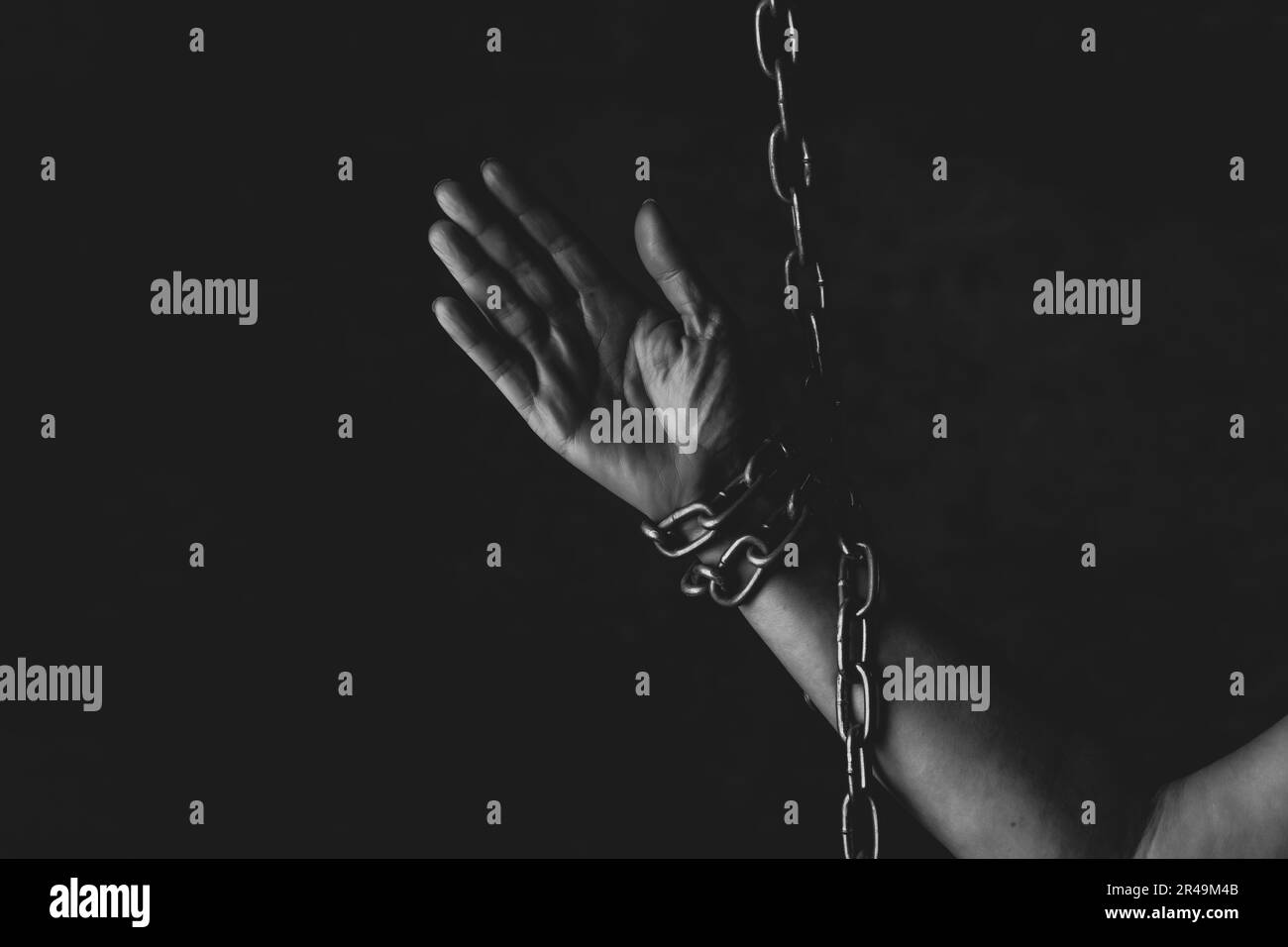 A person with their fingers gripping a metal chain in a dark setting Stock Photo