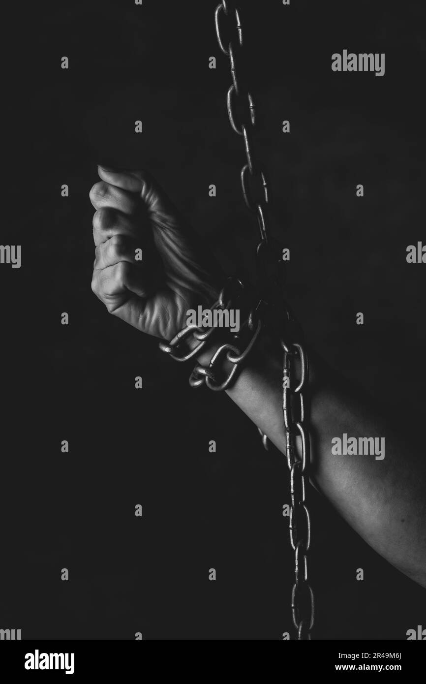 A person with their fingers gripping a metal chain in a dark setting Stock Photo