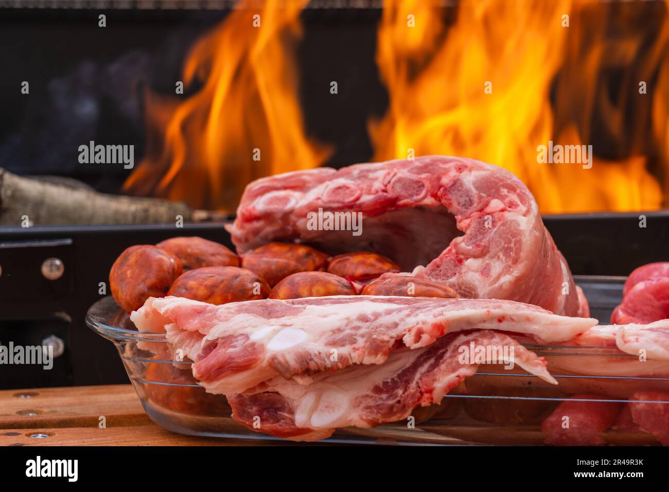 An array of raw meats and sausage near a burning grill with flames Stock Photo