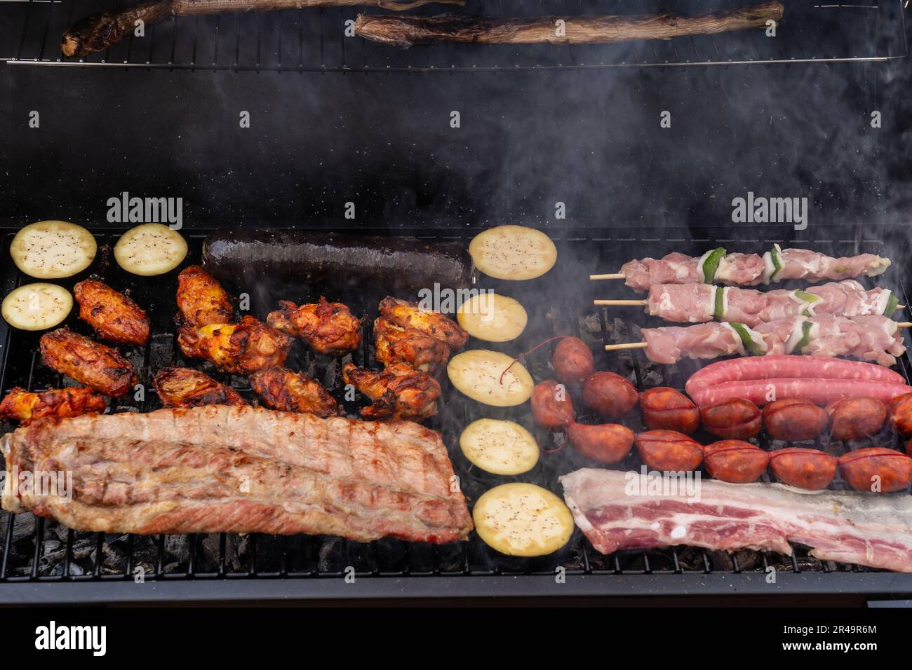 An outdoor barbecue grill with a variety of meats and vegetables cooked on its hot surface Stock Photo