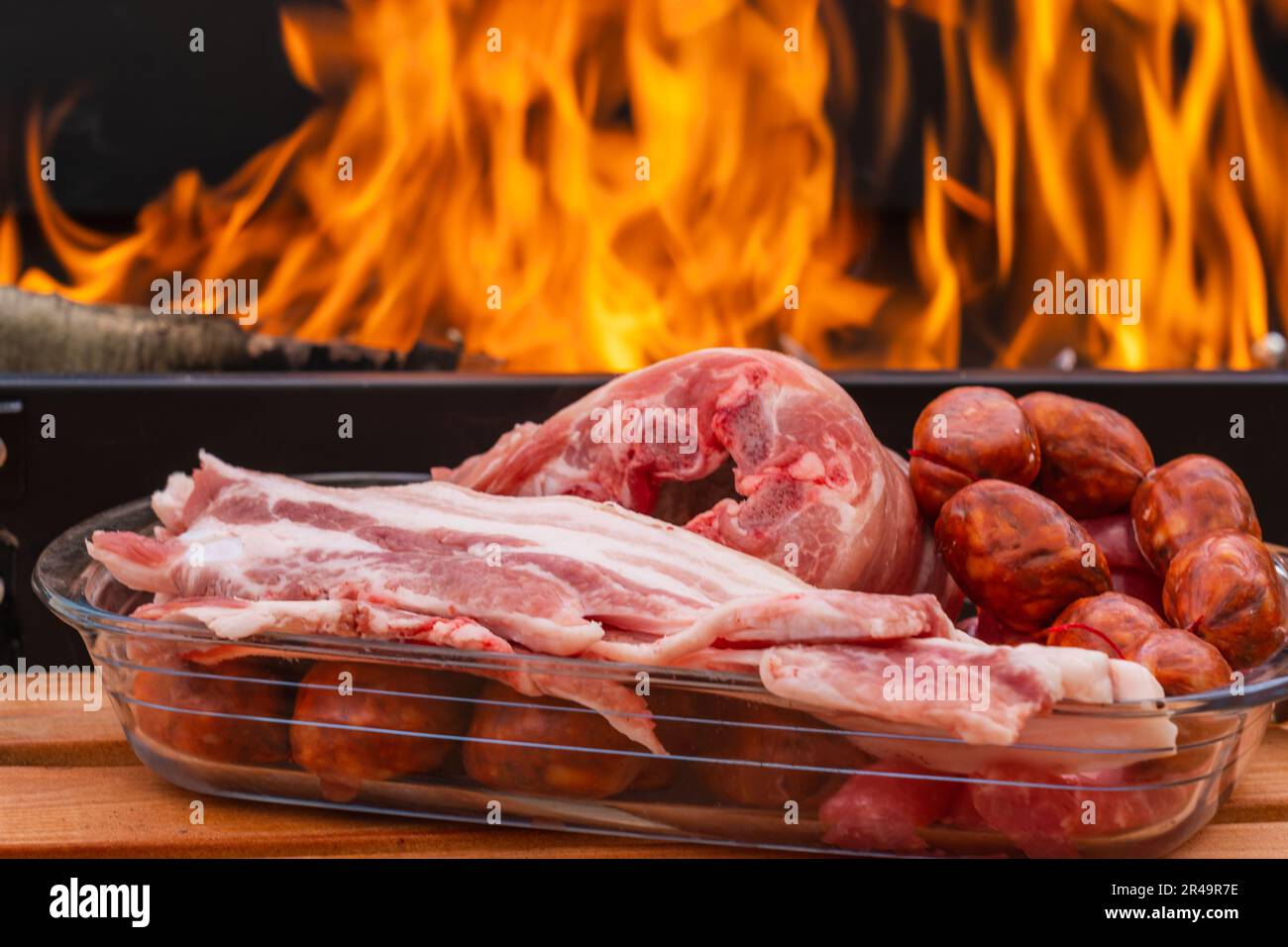 An array of raw meats and sausage near a burning grill with flames Stock Photo