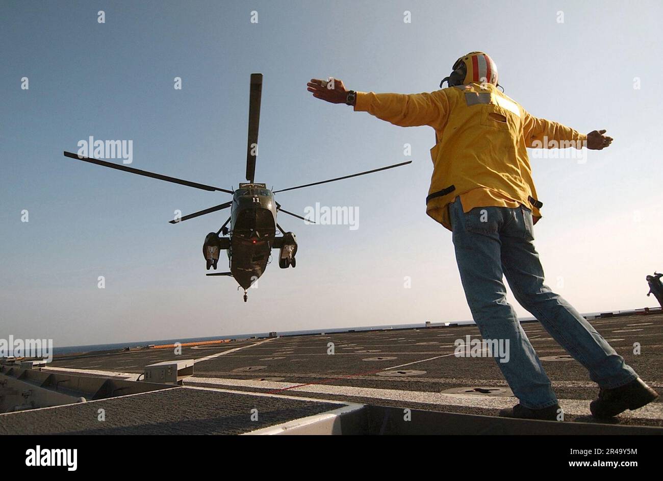 US Navy a civilian mariner assigned to the Military Sealift Command, gives the pilots of a SH-3 Sea King the signal to lift from the flight deck Stock Photo
