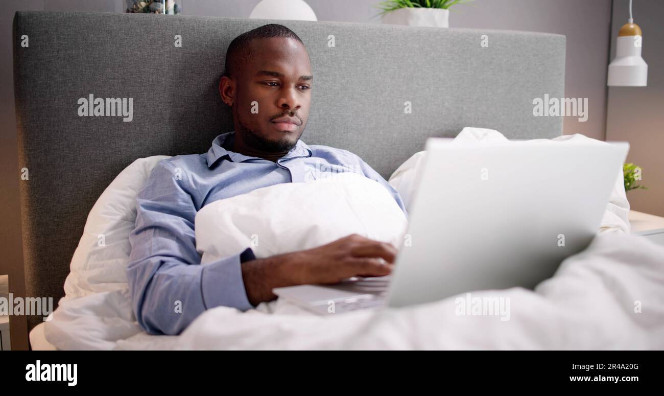 Happy Man Sitting On Bed Using Laptop Stock Photo