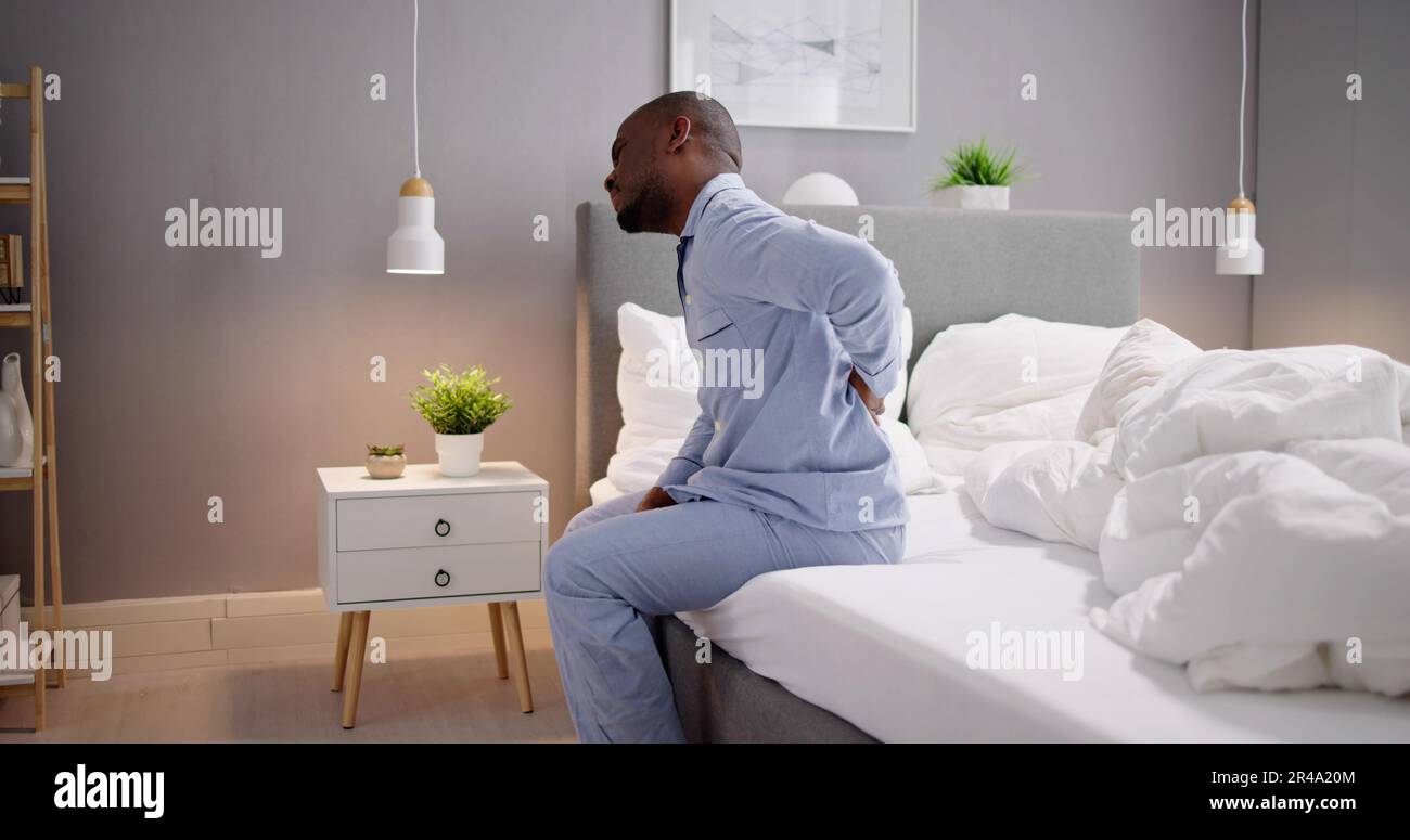 Man Sitting On Bed Suffering From Back Pain Stock Photo - Alamy