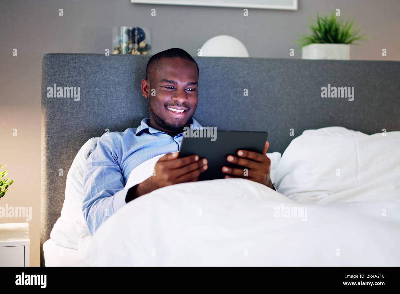 Man Lying On Bed Looking At Illuminated Digital Tablet Stock Photo