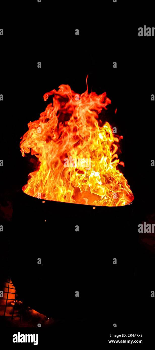 A black bowl sits illuminated by a bright orange flame in a dark setting Stock Photo