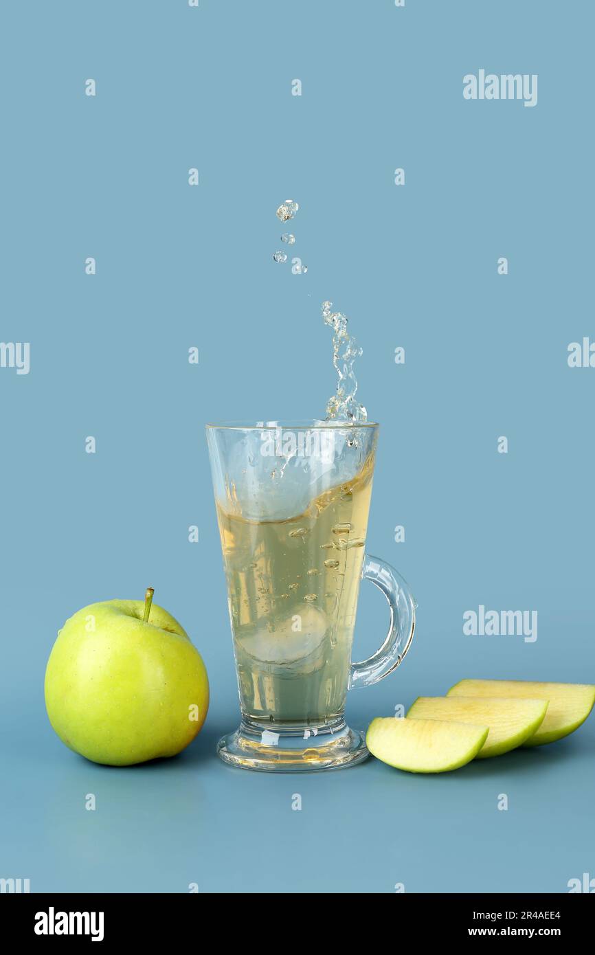 Glass of tasty cider with splashes, ice cube and apples on blue background Stock Photo