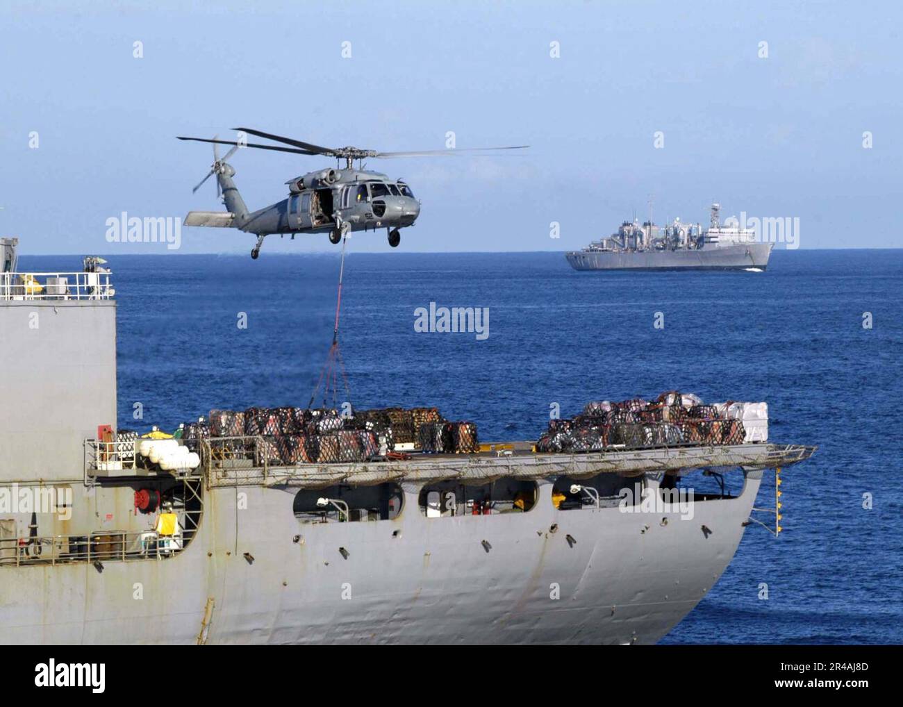 US Navy An MH-60S Knighthawk helicopter lowers cargo onto the deck of the Military Sealift Command (MSC) combat stores ship USNS San Jose (T-AFS 7) Stock Photo