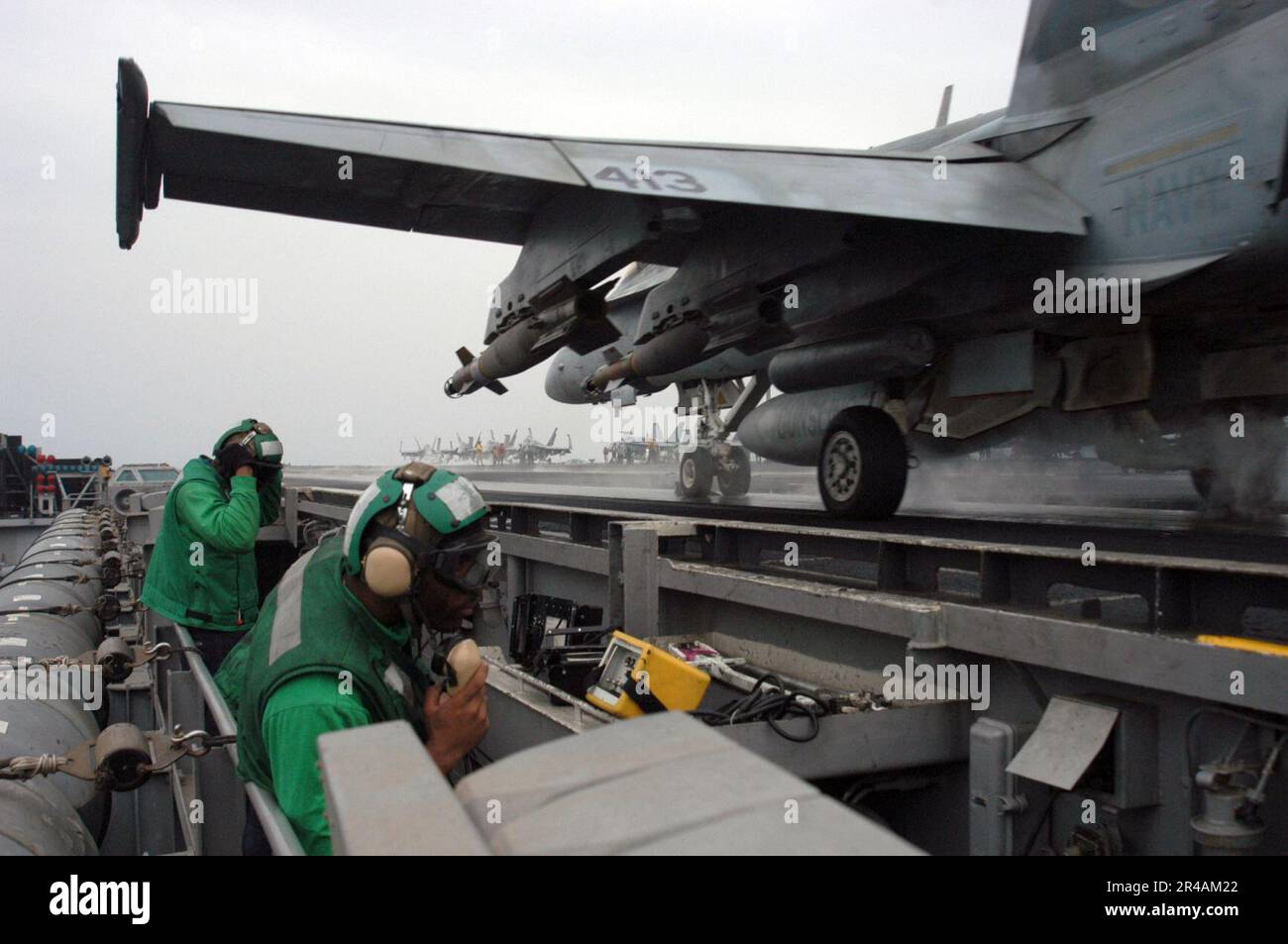 US Navy Air Department Catapult Shooters take cover as an F-A-18C Hornet, assigned to the Gunslingers of Strike Fighter Squadron One Zero Five (VFA-105), is launched off of the flight deck aboard the Nimitz-c Stock Photo