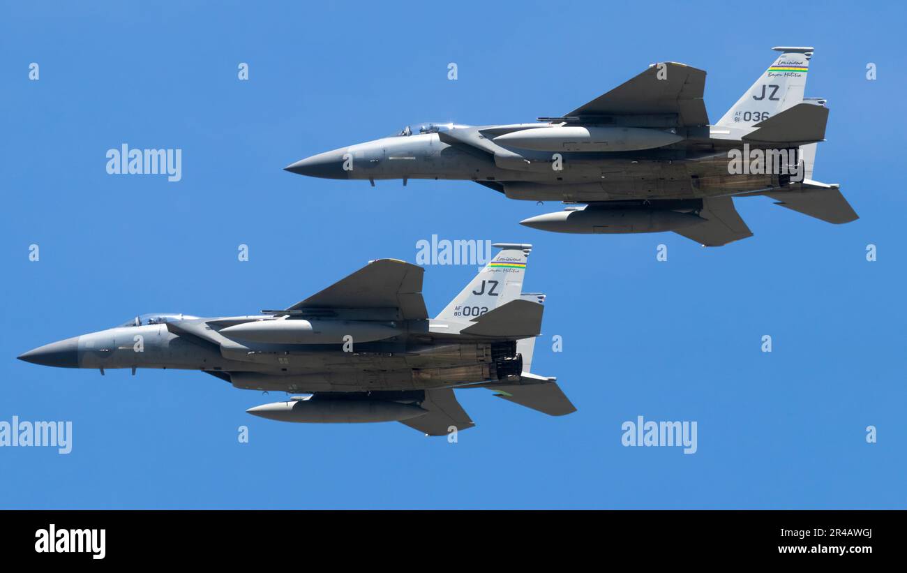 Two military fighter jets in flight formation soaring against a backdrop of a clear blue sky
