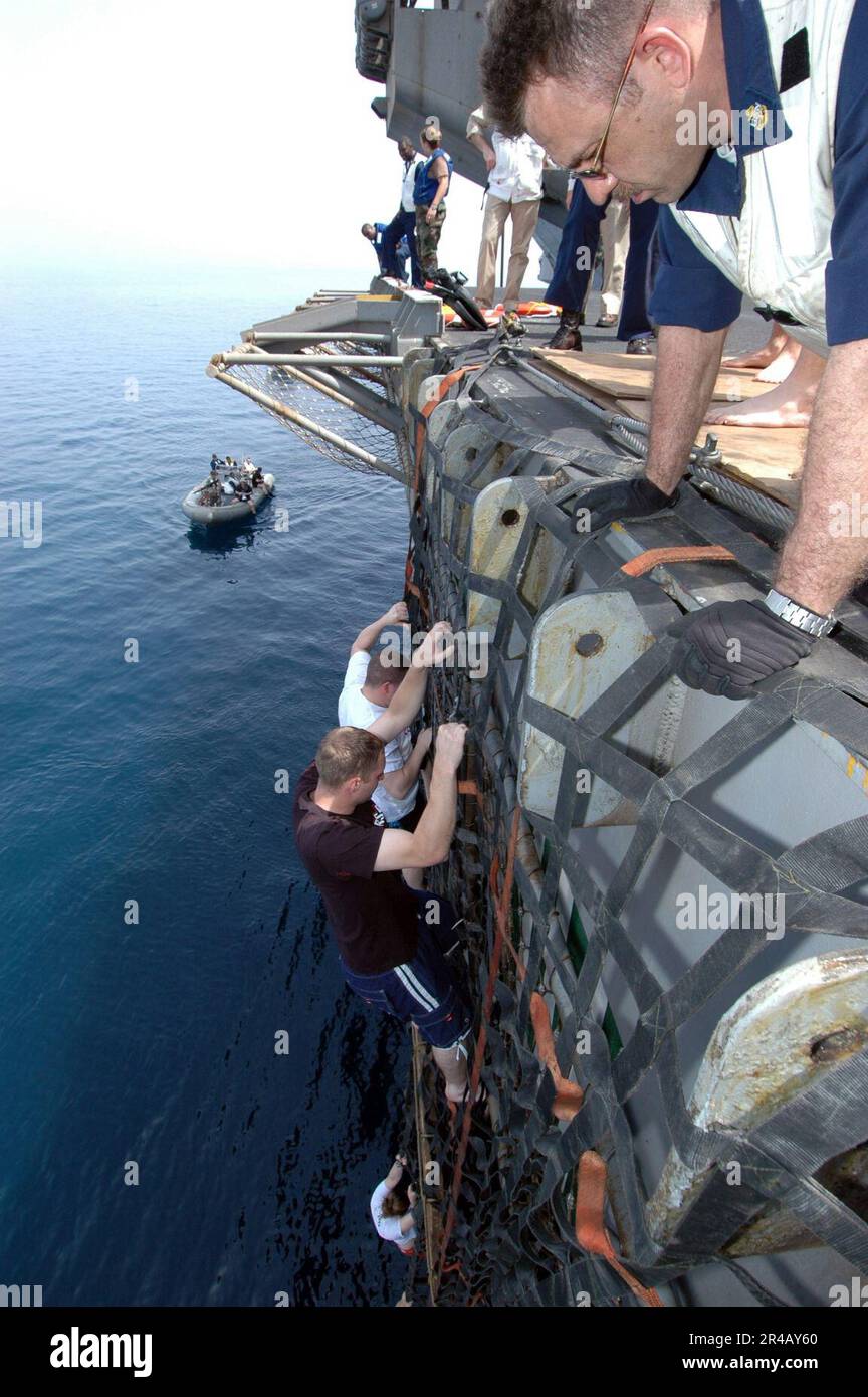 US Navy Sailors and Marines climb down a cargo net and into the cool