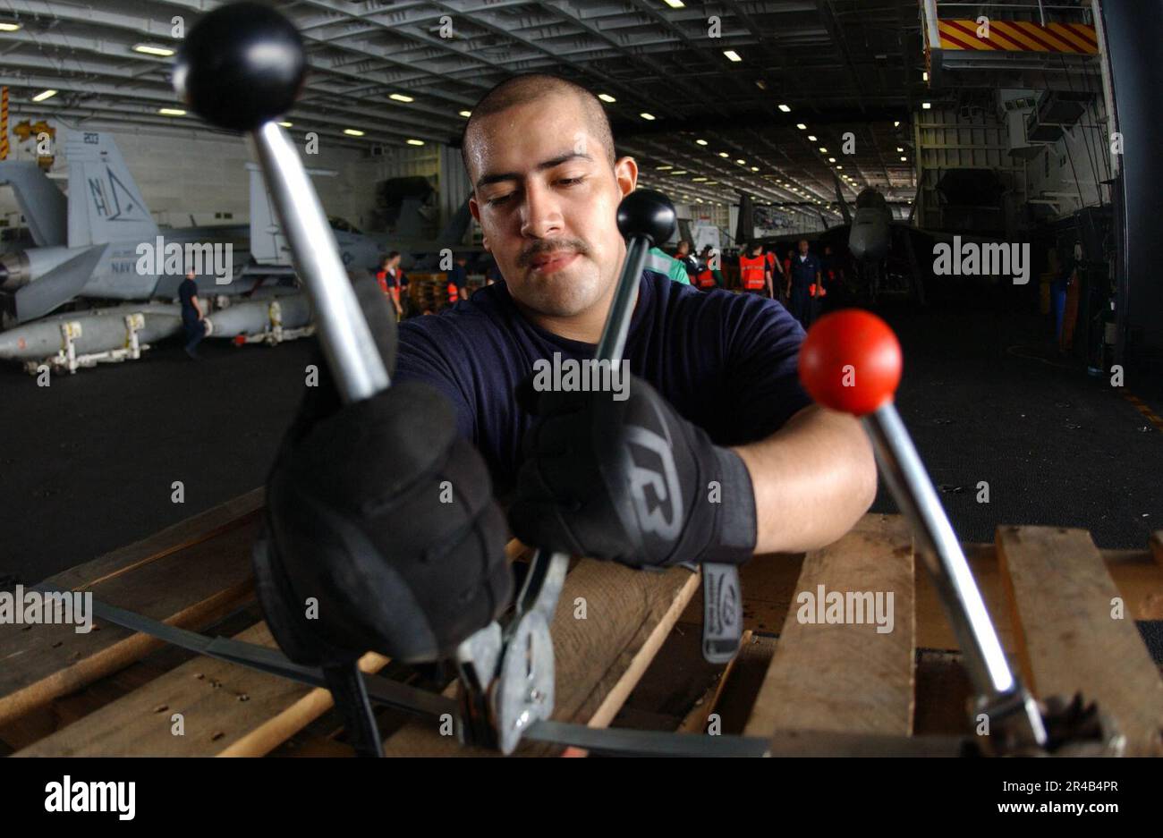 US Navy Storekeeper Seaman bands pallets together with a banding kit in