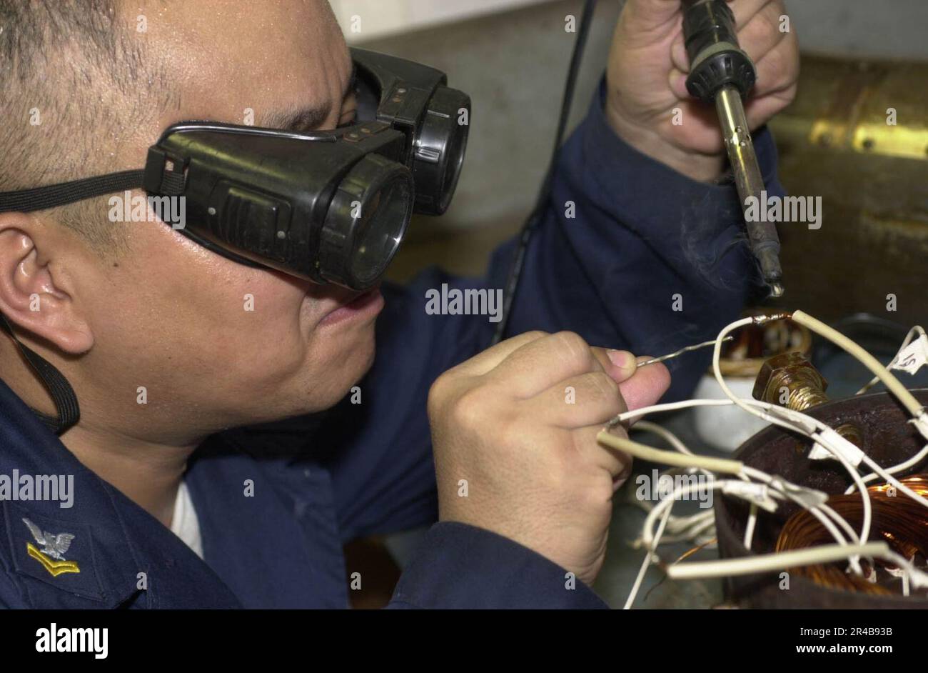 US Navy Electrician's Mate 2nd Class solders the wiring of a vent motor