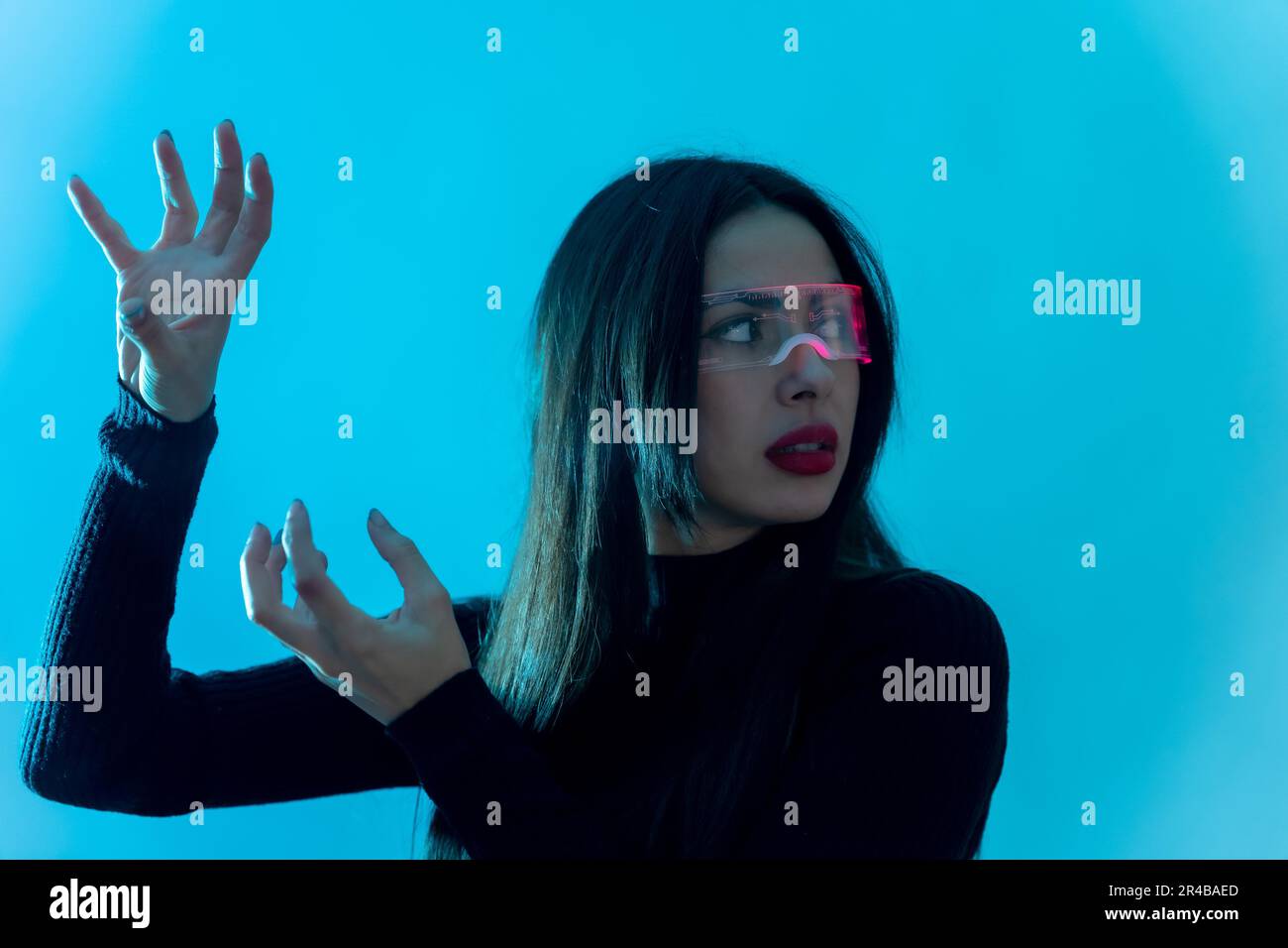 Metaverse technology concept. Woman in futuristic glasses on a blue background. Futuristic Stock Photo