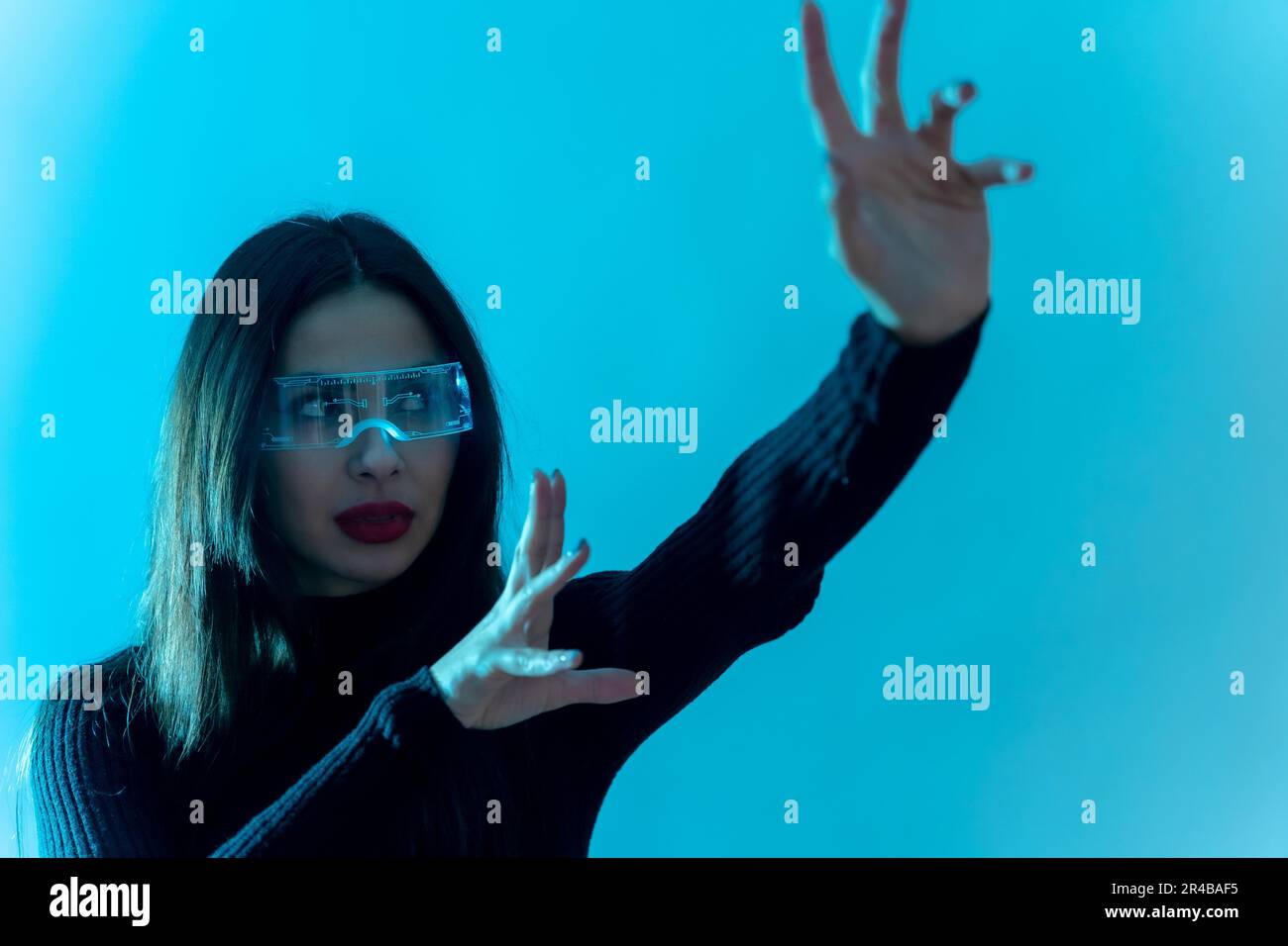 Metaverse technology concept. Woman in futuristic glasses on a blue background. Futuristic Stock Photo