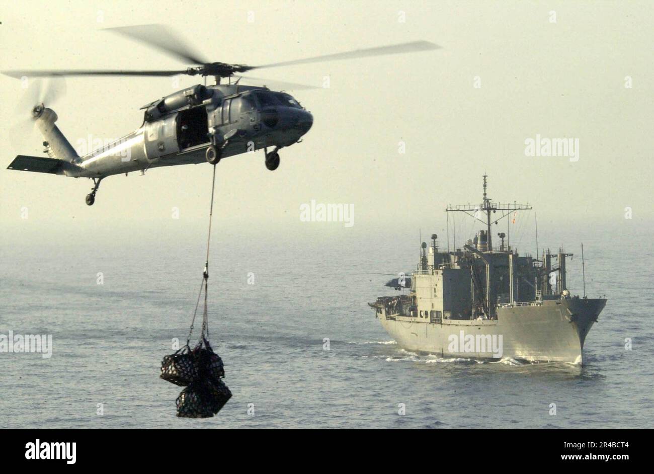 US Navy  An MH-60S Seahawk helicopter carries cargo from the Military Sealift Command (MSC) combat stores ship USNS San Jose (T-AFS 7). Stock Photo