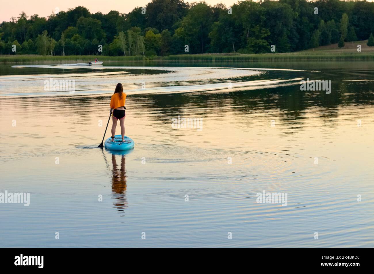 Girl paddling on SUP board on beautiful lake, standing up paddle boarding adventure in Germany lake district Mecklenburg Stock Photo