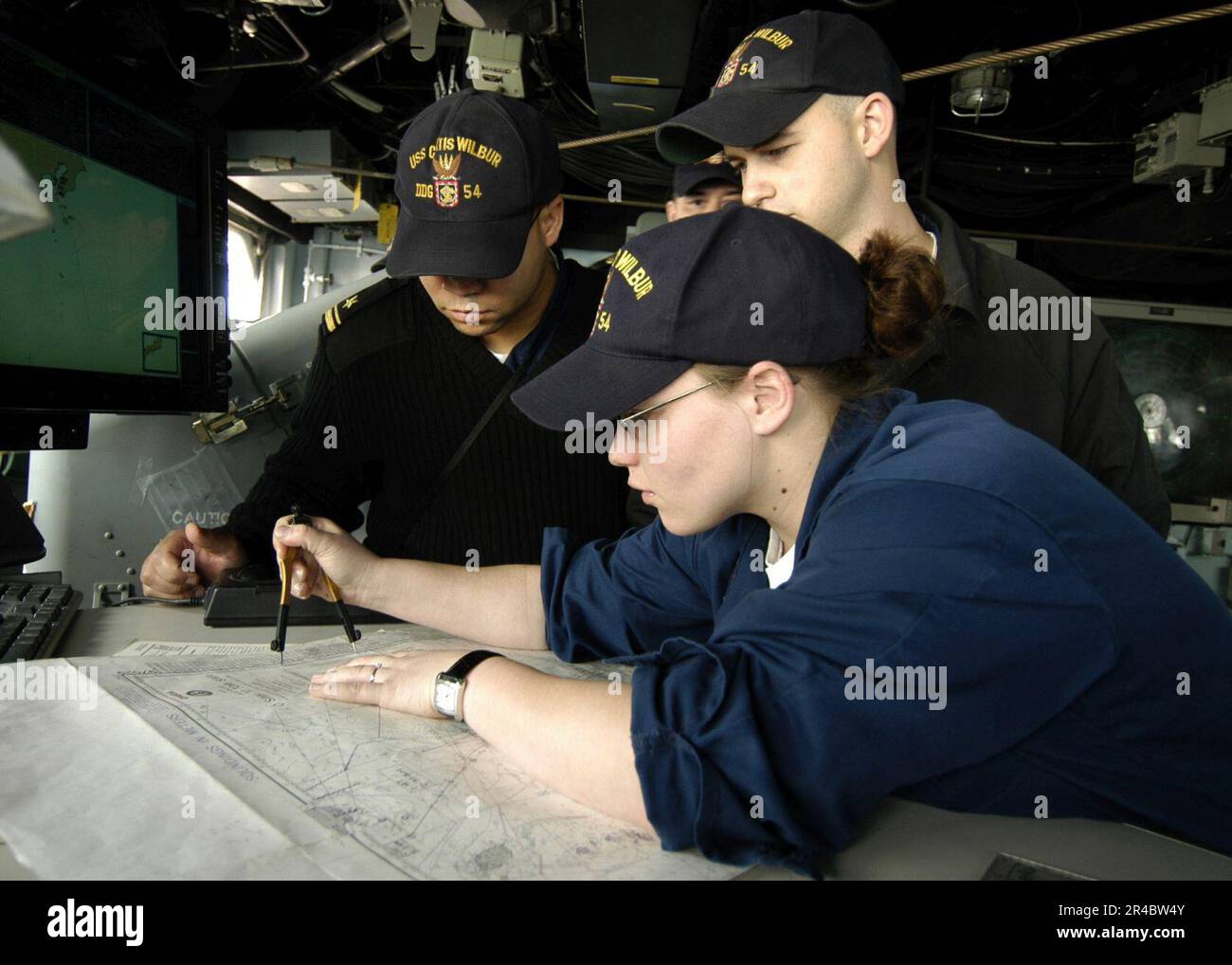 US Navy  Lt. j.g. and Quartermaster Seaman observe the training being held by Quartermaster 2nd Class Rachael H. Hairston as she updates the navigation charts. Stock Photo