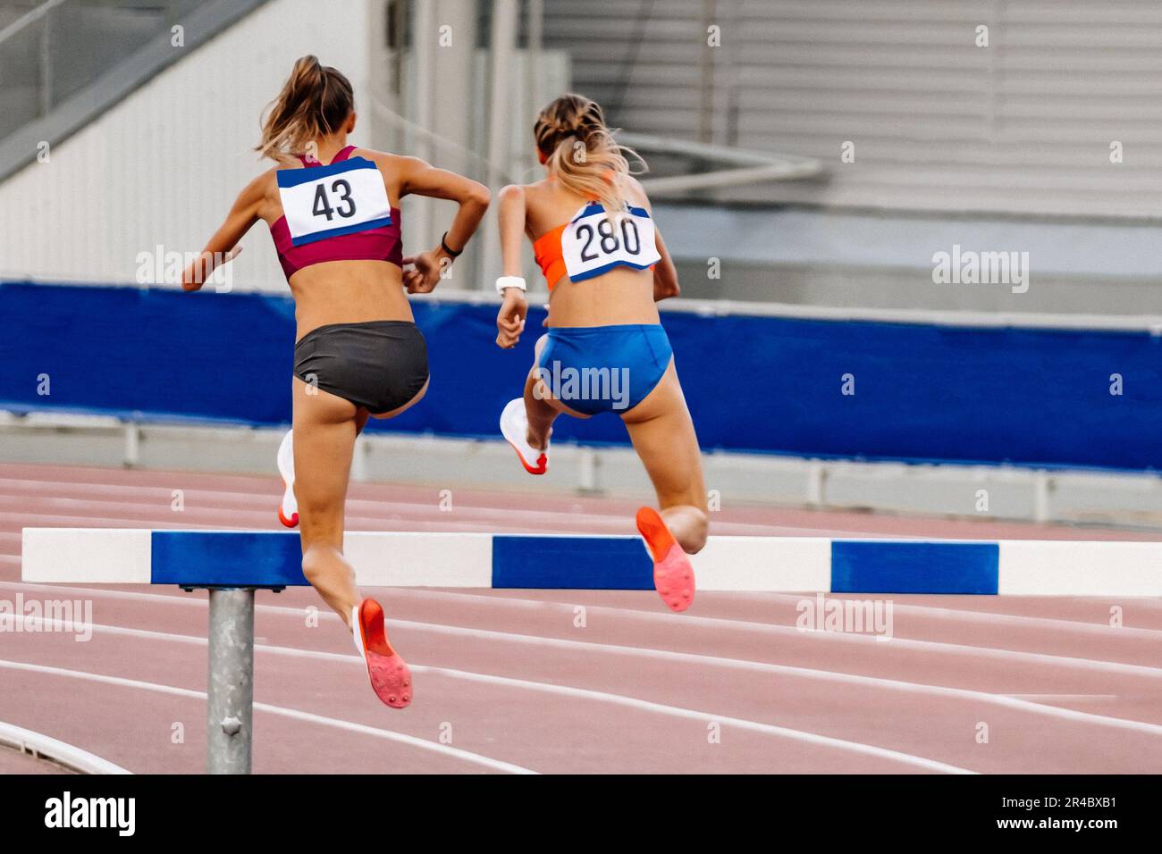 back two woman athlete running steeplechase is obstacle race in summer