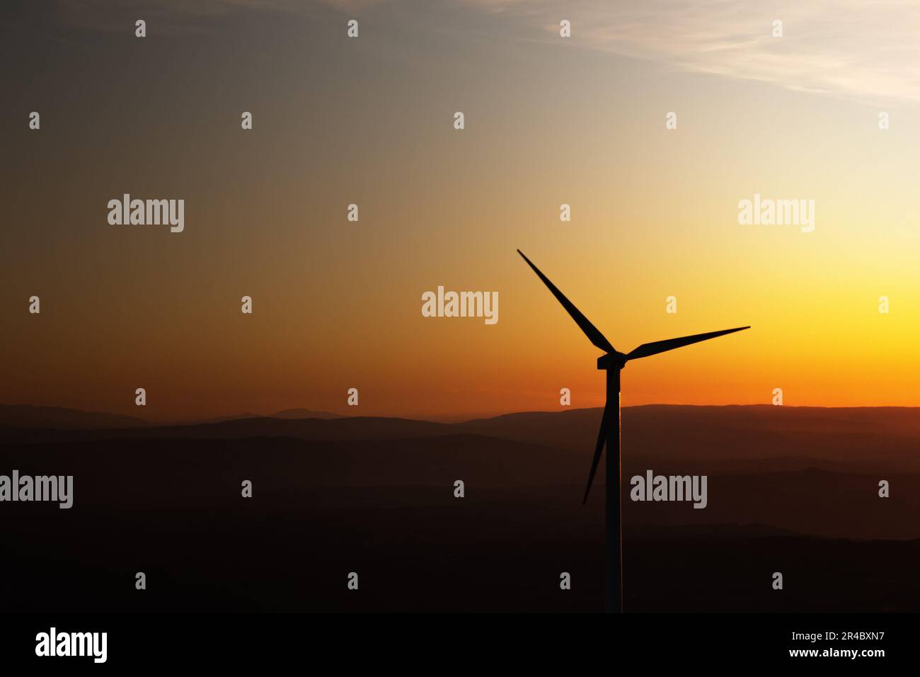 A single wind turbine is silhouetted against an orange sunset sky Stock ...