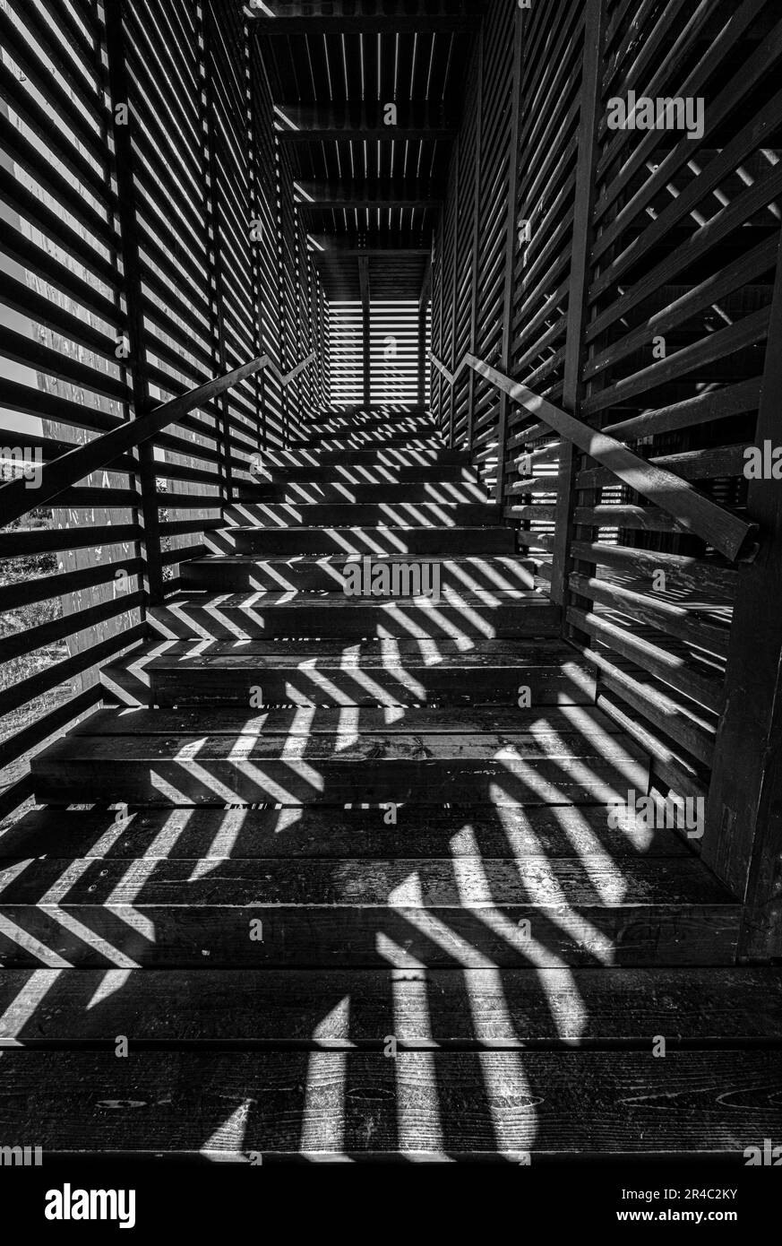 A black and white photograph of a staircase, with sun rays streaming through the window and creating a soft, luminous shadow Stock Photo