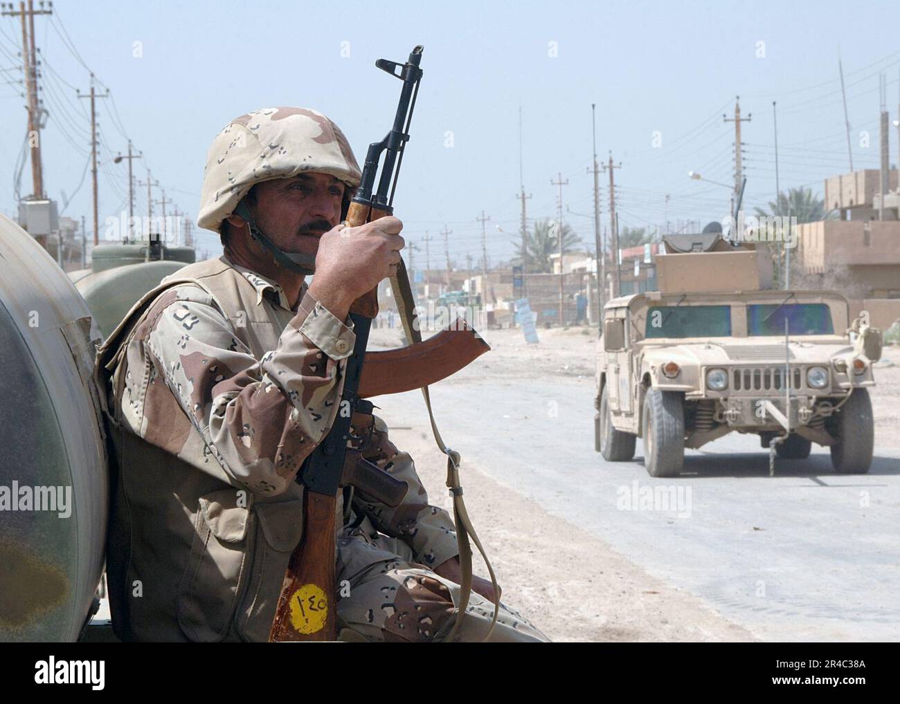 US Navy  Iraqi soldier sits and watches a U.S. Army patrol drive by in their M1114 HMMWV (Humvee) vehicles during counter-insurgency operations. Stock Photo