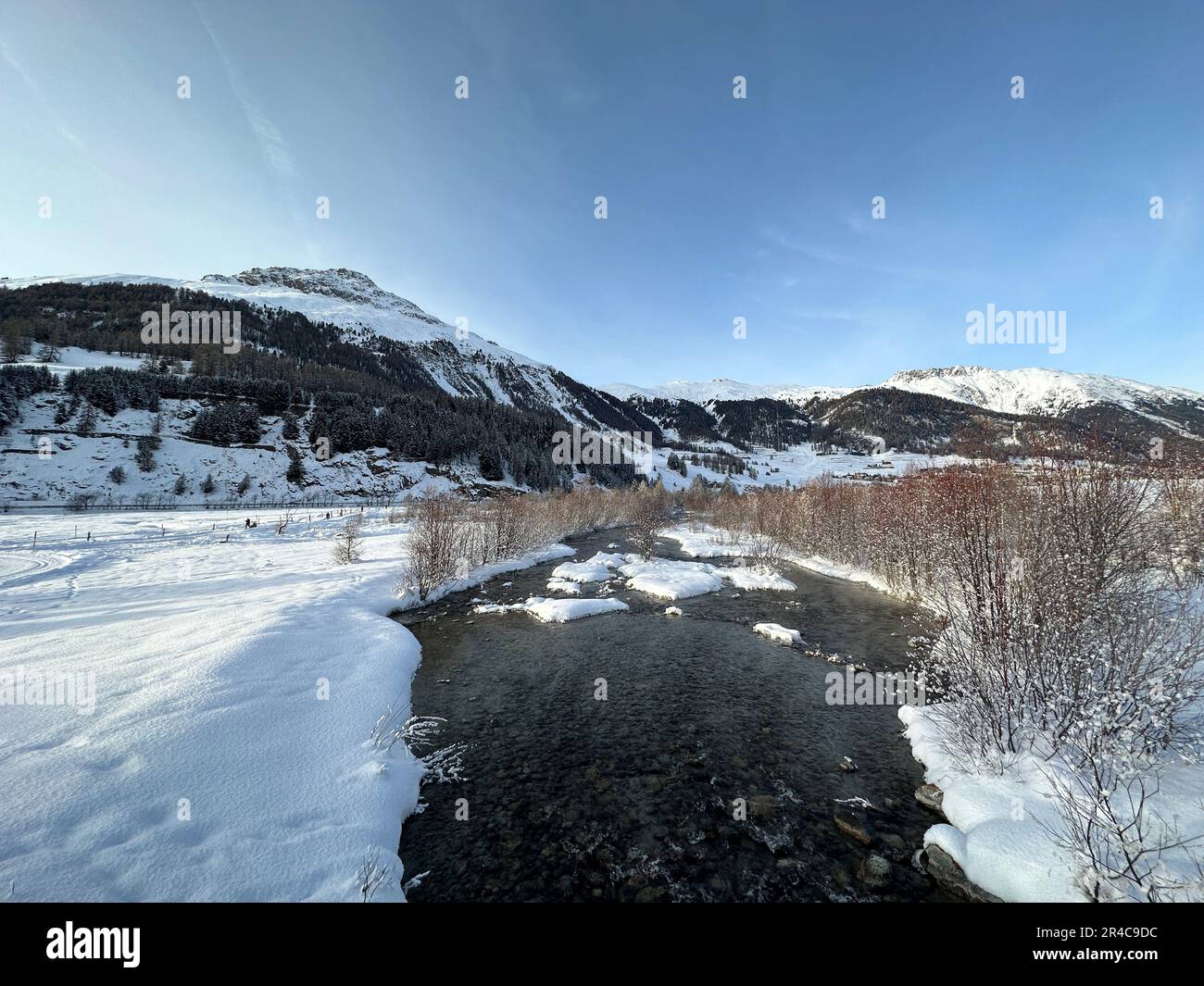 A scenic view of a mountain valley featuring a serene river winding through with patches of snow covering the landscape Stock Photo
