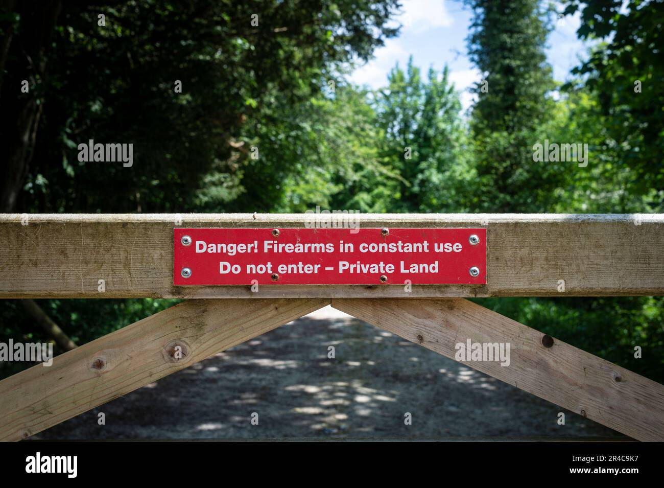 Red warning sign on a gate 'Danger! Firearms in constant use. Do not enter - Private Land'. Stock Photo