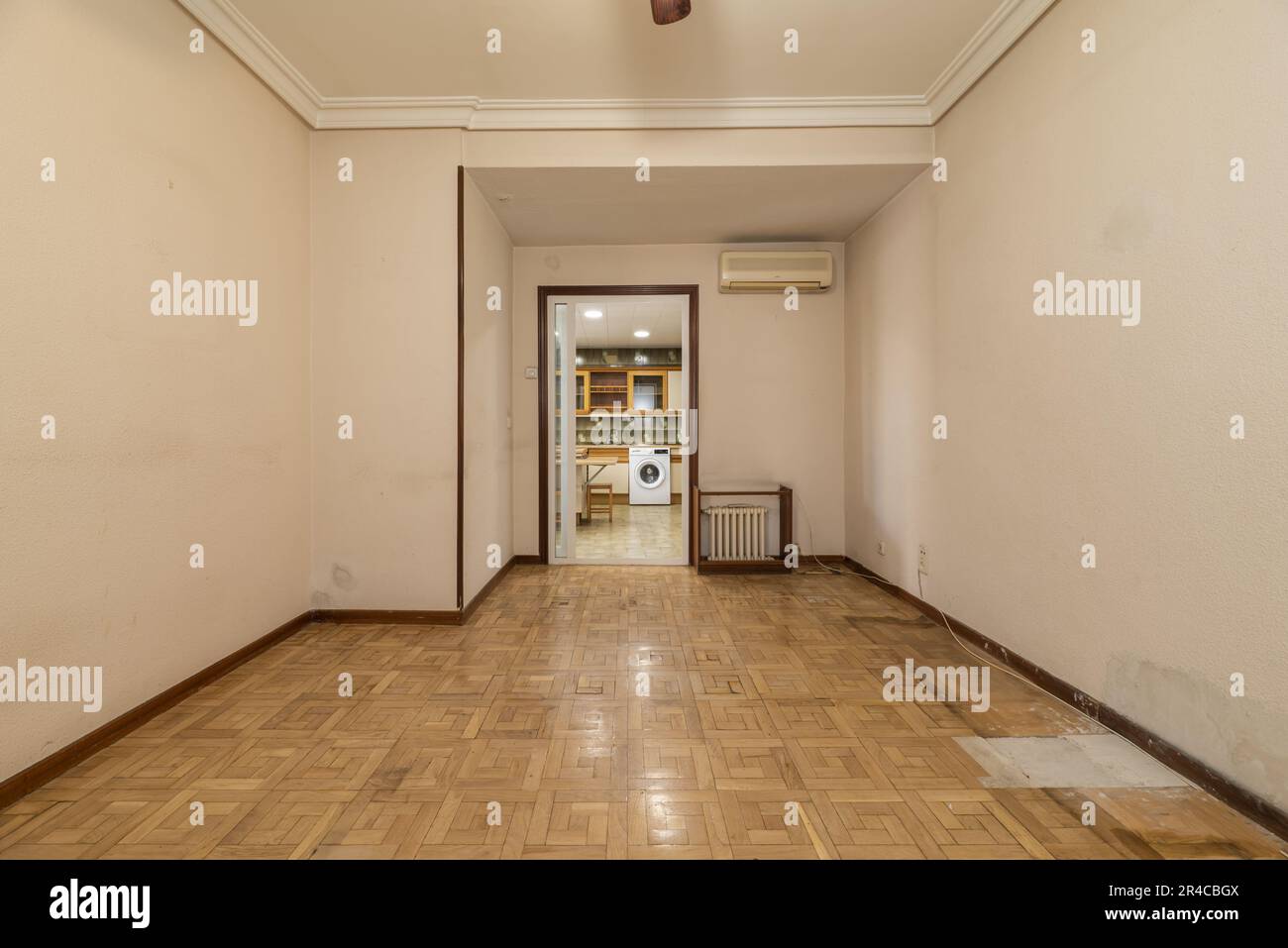 An empty room with damaged oak parquet floors with access to a kitchen Stock Photo