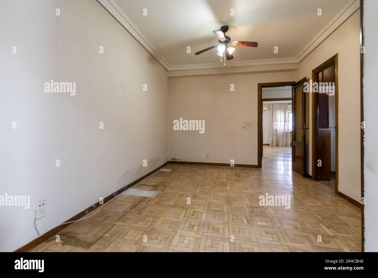 An empty room with a damaged oak parquet floor with access to other rooms and a wooden ceiling fan Stock Photo